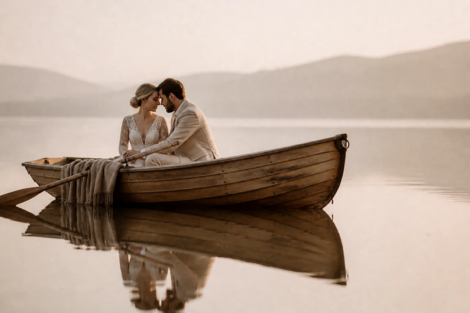 A couple in a rowing boat on a still pale lake at dawn