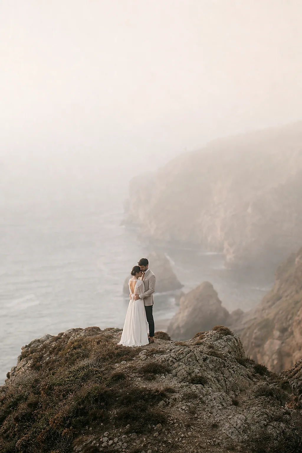 A couple embracing on a misty coastal cliff at dawn